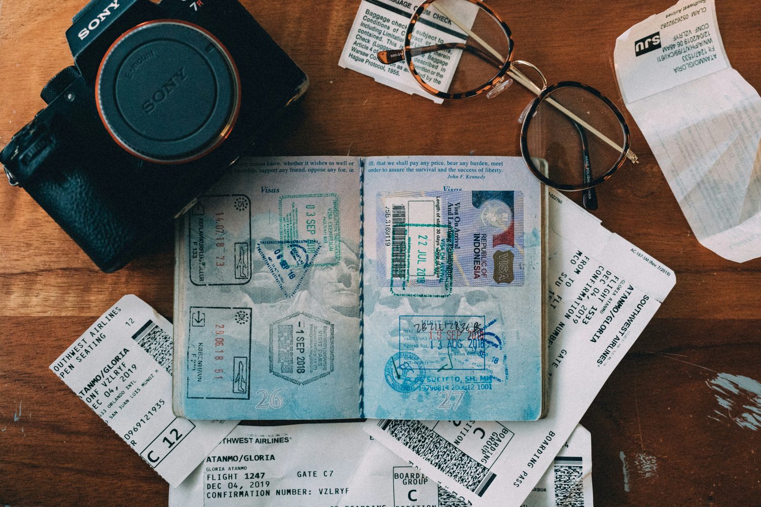 An open passport with visa stamps, a camera, glasses and boarding passes on a wooden table